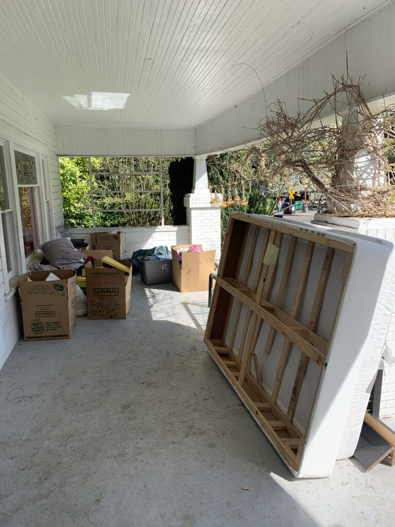 Furniture and household items on a covered porch awaiting junk removal.