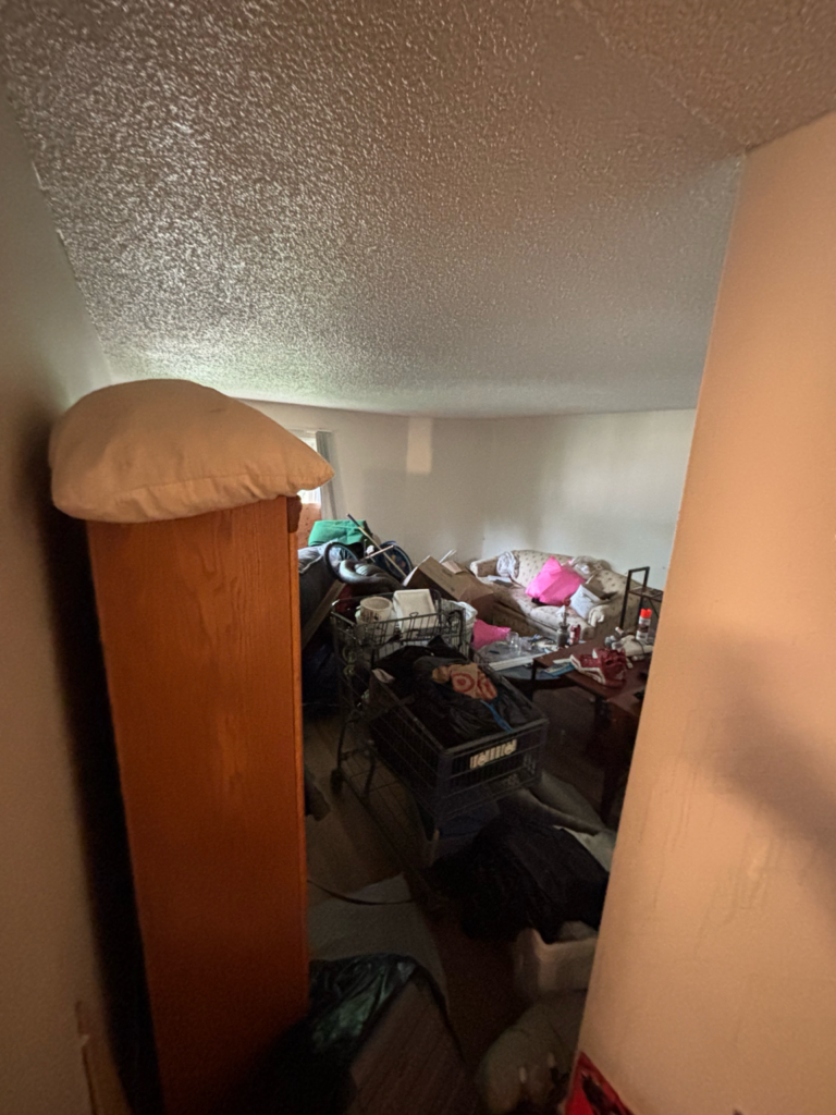 Wooden furniture and piled household belongings in a cluttered room.